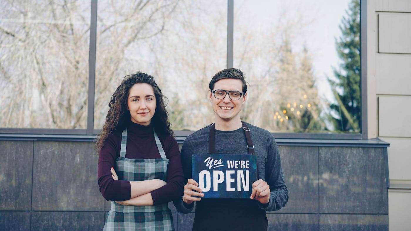Small business owners holding an open sign outside their storefront